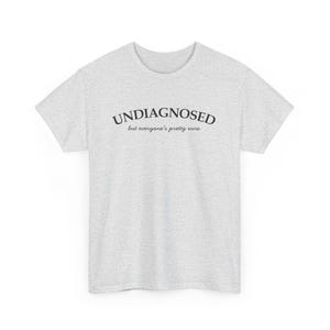 May include: A gray t-shirt with the text "UNDIAGNOSED but everyone's pretty sure" printed on the front.