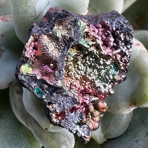 Puede incluir: Primer plano de una roca gris oscura iridiscente con una superficie rugosa y texturizada. La roca tiene una variedad de colores, incluyendo rosa, verde y azul.
