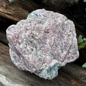 May include: A rough, natural, pink and green crystal with a layered, striated texture. The crystal has a rough, uneven surface and is a natural, unpolished specimen.