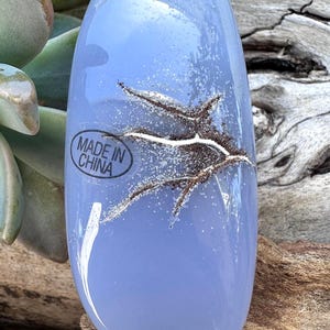 May include: A light blue, oval-shaped glass object with a textured, organic design. The glass has a frosted appearance with a network of brown and white lines. The text "MADE IN CHINA" is visible on the object.