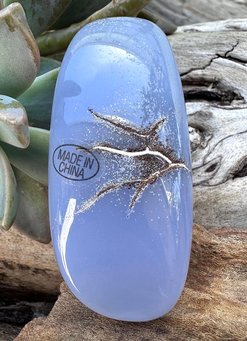May include: A light blue, oval-shaped glass object with a textured, organic design. The glass has a frosted appearance with a network of brown and white lines. The text "MADE IN CHINA" is visible on the object.