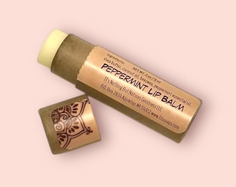 May include: A brown cardboard tube with a gold label that reads "Peppermint Lip Balm" and lists the ingredients: shea butter, coconut oil, beeswax, and peppermint essential oil. The tube is 3 oz/9 ml and is made by TT's Nothing But Nature's Goodness LLC. The tube is open and the lip balm is visible.