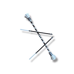 May include: Two baton twirling props featuring a black and white spiral pattern along the shaft. Each baton has a white fringed end and a solid black handle section. The design includes alternating black and white bands near the fringed tips.