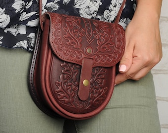 May include: A brown leather crossbody bag with an intricate floral design. The bag has a flap closure with a brass button and a small pocket on the front.
