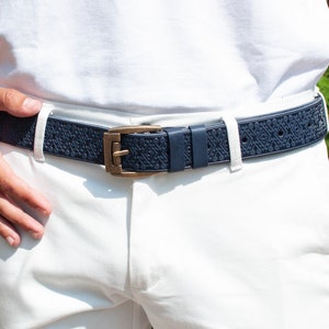 Op de afbeelding: Een donkerblauwe riem met een getextureerd ontwerp en een gouden gesp. De riem wordt gedragen over een witte broek.