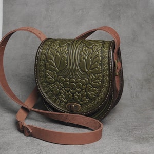 May include: A green leather crossbody bag with an embossed floral design. The bag has a brown leather strap and a metal clasp.