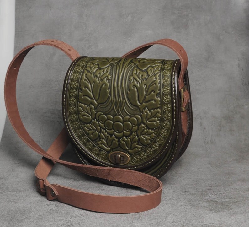 May include: A green leather crossbody bag with an embossed floral design. The bag has a brown leather strap and a metal clasp.