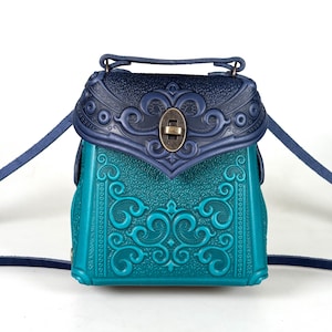 May include: A small, teal and navy blue leather handbag with an ornate, embossed design. The bag has a flap closure with a metal clasp and a single shoulder strap.