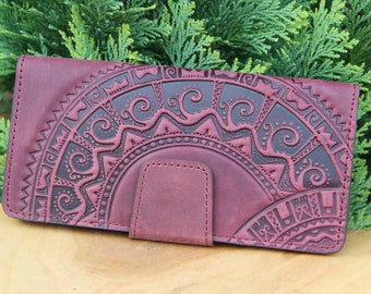 May include: A burgundy leather wallet with an intricate embossed design. The design features a circular pattern with swirls and geometric shapes.