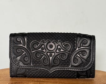 May include: A black leather wallet with intricate floral embroidery. The wallet has a flap closure and a textured design.