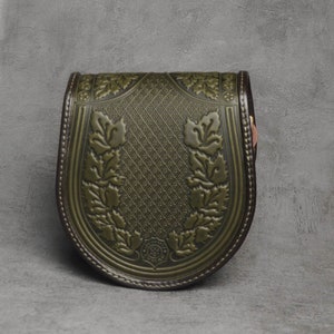 May include: A green leather bag with a floral design and a brown leather trim. The bag has a curved shape and a flap closure.