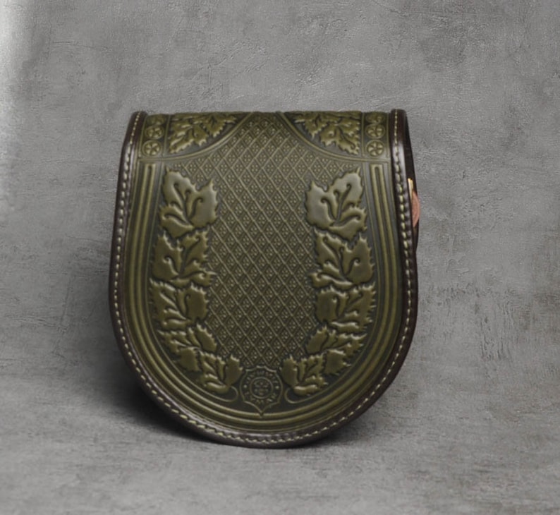 May include: A green leather bag with a floral design and a brown leather trim. The bag has a curved shape and a flap closure.