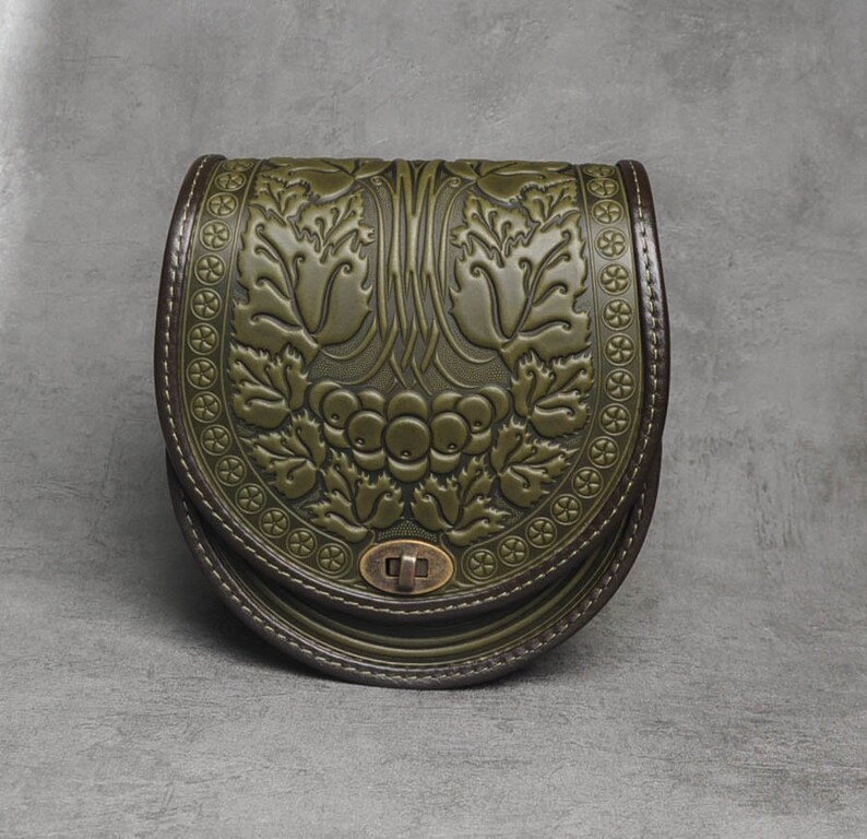 May include: A green leather satchel bag with a floral embossed design. The bag has a flap closure with a metal clasp.
