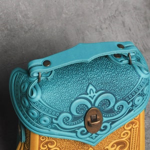 Puede incluir: Un bolso de cuero azul turquesa con intrincados dise&ntilde;os florales en relieve y un cierre de lat&oacute;n. El bolso tiene un asa superior y un cierre de solapa.