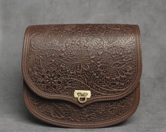 May include: A brown leather satchel bag with a floral embossed design and a gold metal clasp.