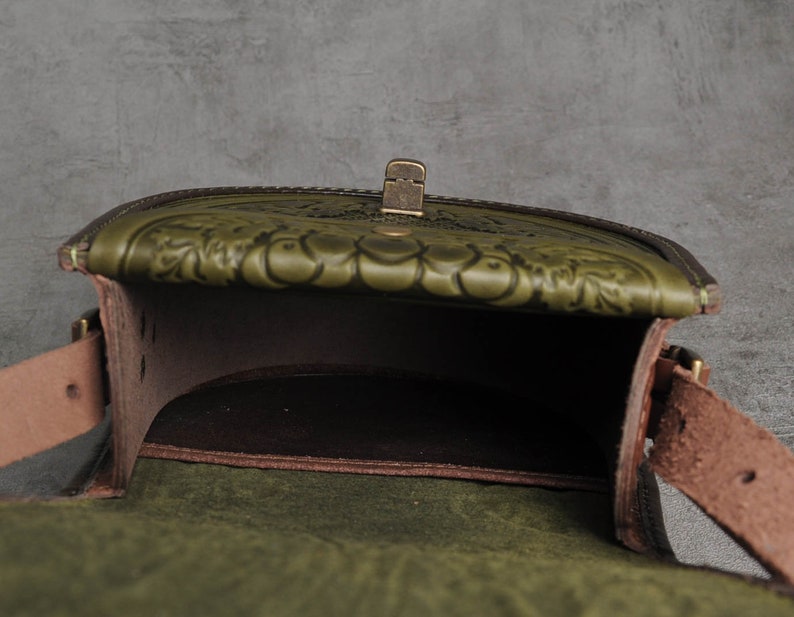 May include: A green leather satchel bag with a flap closure and a brass buckle. The bag has a floral embossed design and a brown leather lining.