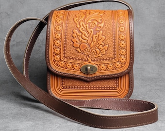 May include: A brown leather crossbody bag with a floral design and a brown strap. The bag has a flap closure with a metal clasp.