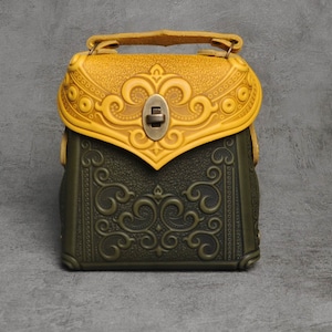 Può includere: Una piccola borsa a mano in pelle verde e gialla con intricati motivi floreali in rilievo sul davanti. La borsa ha un manico superiore e una chiusura a lembo con una fibbia in metallo.