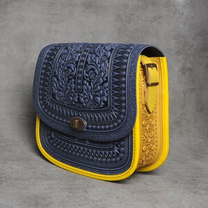 May include: A blue and yellow leather satchel bag with a floral embossed design. The bag has a flap closure with a brass buckle and a yellow strap.