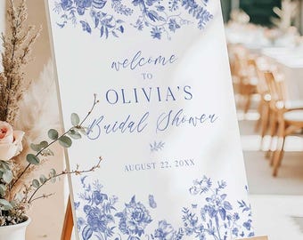 May include: A white sign with blue floral designs and the text "Welcome to Olivia's Bridal Shower August 22, 20XX".