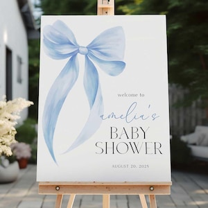 May include: A blue watercolor bow with a white background. The text "Welcome to Amelia's Baby Shower" is printed below the bow. The date "August 20, 2025" is printed below the text.