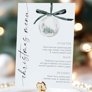 May include: A white Christmas menu card with elegant script, featuring a watercolor ornament illustration and a dark green ribbon. The menu lists a starter, main course, and dessert for a holiday meal.