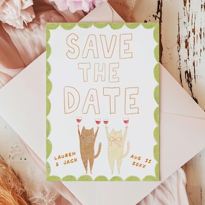 May include: A white "Save the Date" card with a green scalloped border, featuring two cartoon cats toasting with wine glasses. The card is inside a pink envelope, with text that reads "Lauren & Jack" and "Aug 11 20xx".