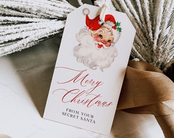 May include: A white gift tag with a vintage illustration of Santa Claus. The tag has red cursive writing that says "Merry Christmas" and "From Your Secret Santa".
