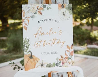 May include: A white welcome sign with a watercolor design of pumpkins, leaves, and flowers. The text on the sign reads "Welcome to Amelia's 1st birthday, Nov 22, 20XX".