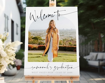May include: White welcome sign with a black arch and the text "Welcome to" and "savannah's graduation" with the text "West Valley High - Class of 20XX" below. A photo of a person in a graduation gown is in the arch.
