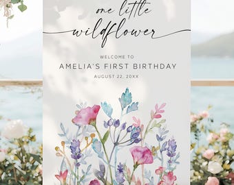 May include: A white sign on a wooden easel with the text "one little wildflower" and "Welcome to Amelia's First Birthday August 22, 20XX". The sign features watercolor floral art in pink, blue, and purple.