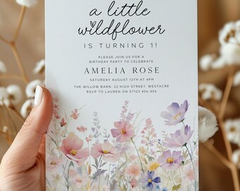 May include: A white invitation card with the text "a little wildflower is turning 1!" and floral illustrations in pink, purple, and blue. The card also includes the name "Amelia Rose" and party details.