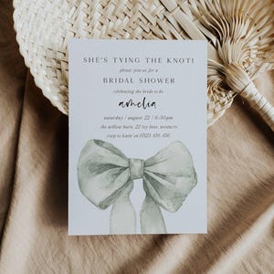 Pu&ograve; includere: Un invito a un bridal shower bianco con un'illustrazione ad acquerello di un fiocco verde chiaro. Il testo recita "She's tying the knot!" e include i dettagli dell'evento, tra cui il nome della sposa, la data, l'ora e il luogo.