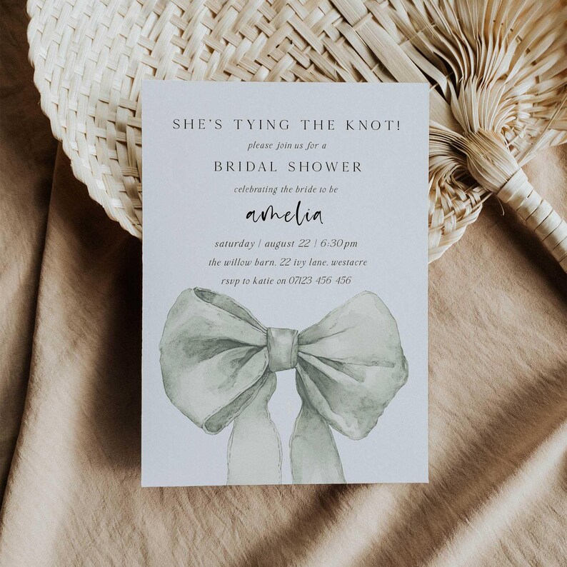 Pu&ograve; includere: Un invito a un bridal shower bianco con un'illustrazione ad acquerello di un fiocco verde chiaro. Il testo recita "She's tying the knot!" e include i dettagli dell'evento, tra cui il nome della sposa, la data, l'ora e il luogo.