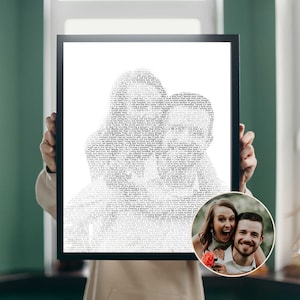 May include: A framed black and white print featuring a silhouette of two people kissing, filled with song lyrics. A small, circular photo of a smiling couple is in the lower right corner. The print is held up by a person.