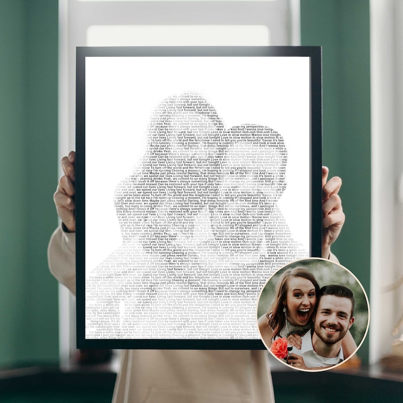 May include: A framed black and white print featuring a silhouette of two people kissing, filled with song lyrics. A small, circular photo of a smiling couple is in the lower right corner. The print is held up by a person.