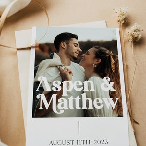 May include: A wedding announcement card with a photo of a couple looking at each other. The card is white with black text that says "Aspen & Matthew" and "August 11th, 2023". The website address "www.aspenandmatthew.com" is printed at the bottom of the card.