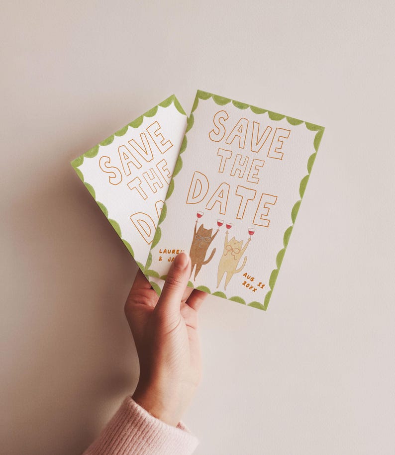 May include: Two white "Save the Date" cards with gold lettering and a green scalloped border. The cards feature illustrations of cats toasting with wine glasses. The date "Aug 11 20XX" is printed on the card.