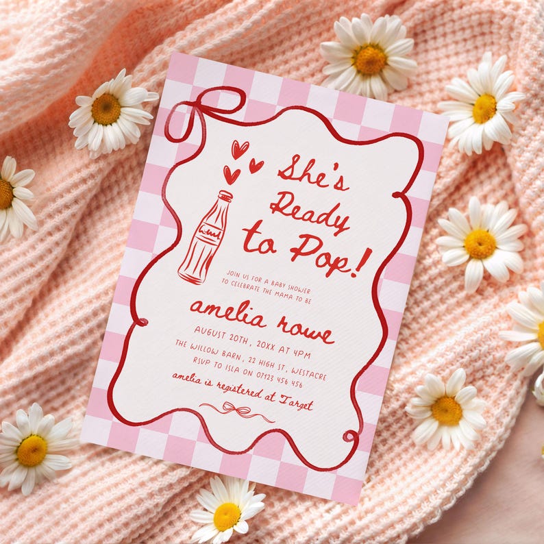 May include: A baby shower invitation with a pink gingham background and red accents. The invitation reads "She's Ready to Pop!" and includes details for the event, such as the date, time, and location. White daisies are scattered around the invitation.