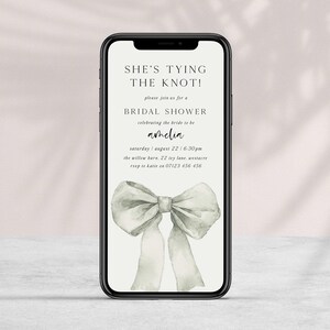 Pu&ograve; includere: Un invito digitale per un addio al nubilato con un'illustrazione ad acquerello di un fiocco bianco. Il testo recita "She's tying the knot!" e include il nome della sposa, Amelia, la data, l'ora e il luogo dell'evento.