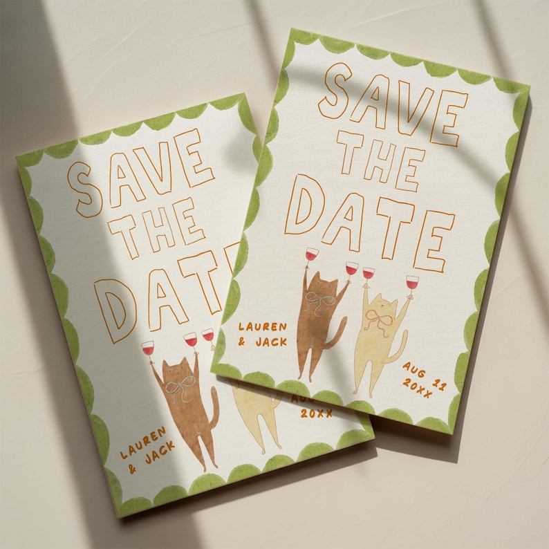 May include: Two "Save the Date" cards with a light green scalloped border. The cards feature the text "SAVE THE DATE" in orange, along with illustrations of cats toasting with wine glasses. The names "LAUREN & JACK" and a date are also included.