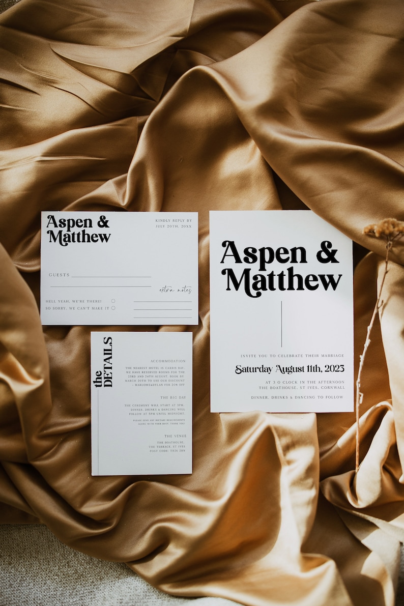 May include: White wedding invitation cards with black text. The top card says "Aspen & Matthew" in a bold, retro font. The bottom card has the details of the wedding, including the date, time, and location. The text reads "Invite you to celebrate their marriage Saturday August 11th, 2023 at 3 o'clock in the afternoon The Boathouse, St Ives, Cornwall Dinner, drinks & dancing to follow."