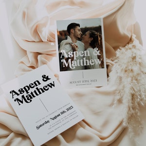 May include: A white wedding invitation with black text that reads "Aspen & Matthew" and "Saturday August 11th, 2023". The invitation also includes the couple's website address. A smaller photo card with the same text and a photo of the couple is on top of the invitation.