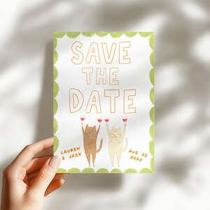 May include: A watercolor "Save the Date" card featuring two cartoon cats toasting with wine glasses. The card has a green scalloped border and includes the names "Lauren & Jack" and the date "Aug 11 20XX".