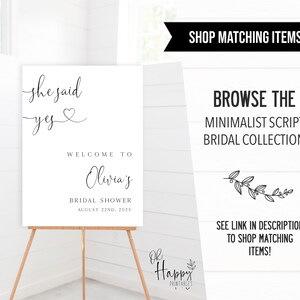 May include: A white printable sign with black text that reads "She said yes" with a heart symbol. The sign also says "Welcome to Olivia's Bridal Shower August 22nd, 2023".