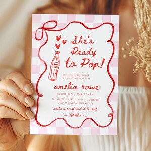 May include: A baby shower invitation with a red and white gingham pattern background. The invitation features red text that reads "She's Ready to Pop!" with a bottle illustration and the name "amelia rowe".
