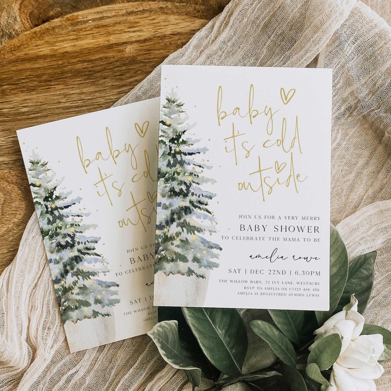 May include: A baby shower invitation with a watercolor illustration of two pine trees with lights. The text reads "baby it's cold outside" with a heart symbol. The invitation is for Amelia Cove and includes the date, time, and location of the shower.