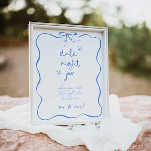 May include: White sign with a blue border and text that says "date night jar" and "share your best date night idea for the new mr & mrs!"
