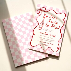 May include: Pink and white checkered baby shower invitation with the text "She's Ready to Pop!" in red script. The invitation features a red border and a drawing of a soda bottle. The back of the invitation has a pink and white checkered pattern.