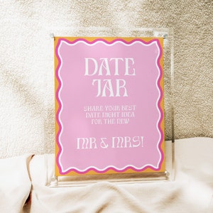 May include: A pink and gold sign with the text "DATE JAR" and "SHARE YOUR BEST DATE NIGHT IDEA FOR THE NEW MR & MRS!" in white lettering.